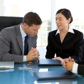 Asian woman providing onsite interpreting to a man at a conference table.
