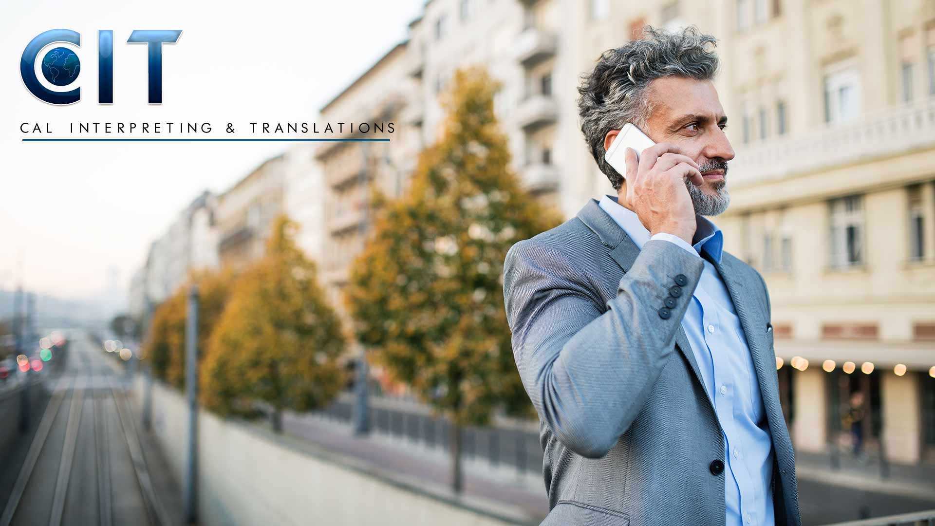 Bearded man in a suit talking on a cell phone while walking down the street.