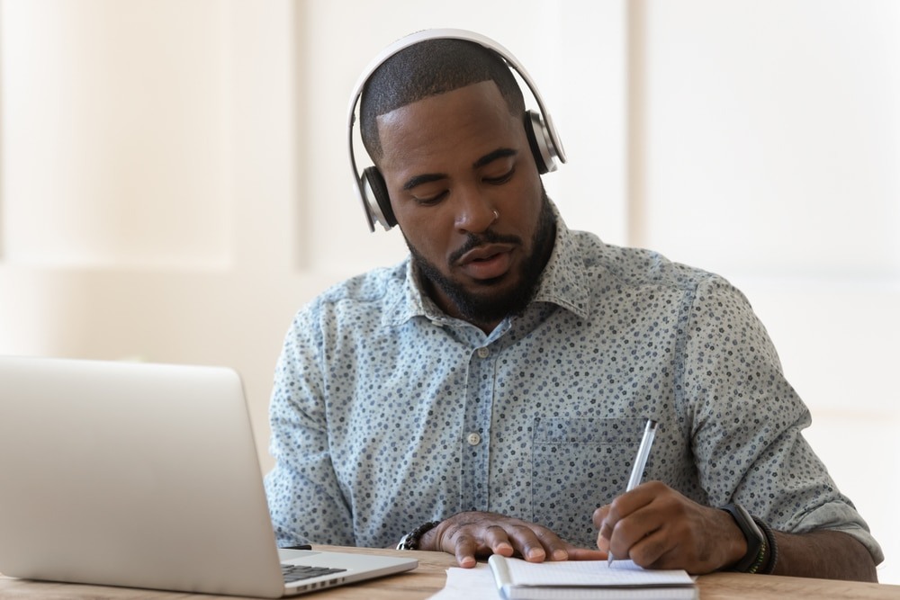 African student wearing headphones listens audio course makes notes
